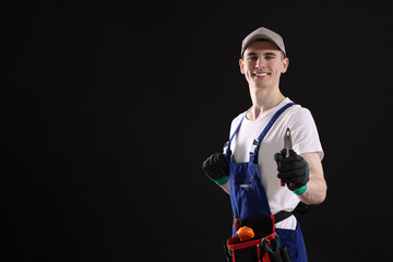 Young man holding pliers on black background, space for text