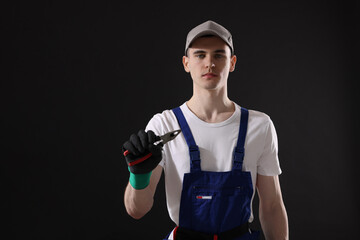 Young man holding pliers on black background, space for text
