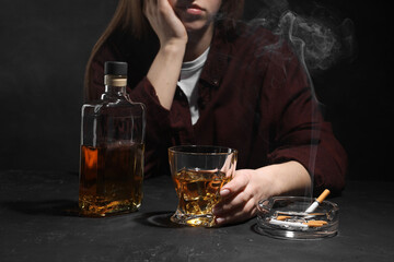Alcohol addiction. Woman with whiskey and smoldering cigarettes at dark textured table, closeup - obrazy, fototapety, plakaty