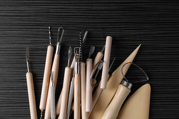 Clay and set of modeling tools on dark gray wooden table, flat lay