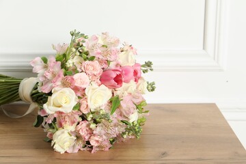 Beautiful bouquet of fresh flowers on wooden table near white wall