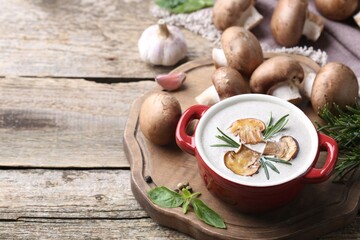 Delicious homemade mushroom soup in ceramic pot and fresh ingredients on wooden table. Space for...