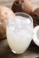 Glass of coconut water, ice cubes and nuts on wooden table