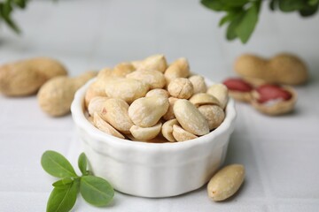 Fresh peeled peanuts in bowl on white tiled table, closeup