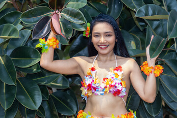 A smiling Hula Hawaii dancer standing by a ficus elastica - rubber tree.