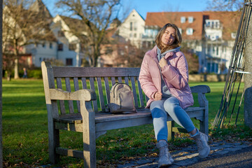 Winter Joy in Bitigheim-Bissingen: Beautiful Girl in Pink Jacket Sitting Amidst Half-Timbered Charm. beautiful girl in a pink winter jacket sitting on a bench in a park, set against the backdrop of