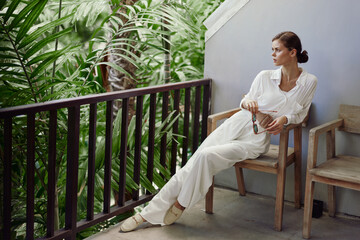 Smiling woman enjoying a tropical vacation on a balcony She stands on a stylish apartment terrace, wearing trendy sunglasses and a happy expression With sunlight casting a warm glow, she relaxes on a