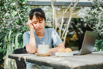 Woman appears stressed or thoughtful while working at an outdoor wooden table with a laptop and...