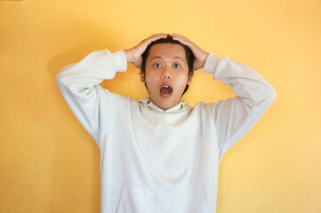 Surprised expression of Asian young man wearing a hoodie with both hands holding his head