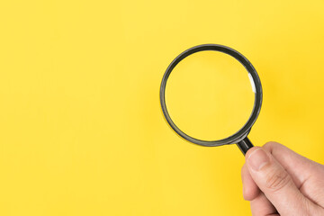 Man hand holding a classic magnifying glass isolated on yellow background - 791213947