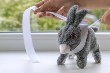 Decorating Plush Bunny by tying bow around neck. Close-up of female hands tying white satin ribbon...