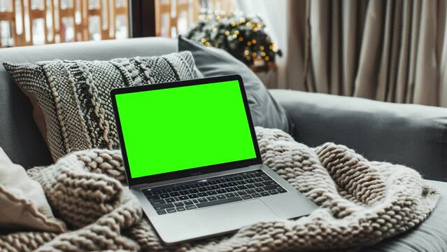 Laptop with blank green screen. Static footage with trees swaying or moving in the wind. Home interior or loft office background, 4k 24fps UHD