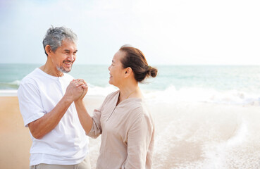 romantic asian senior couple standing at the beach,smiling,looking at each other and hands holding together,concept of elderly people lifestyle,family,relationship,holiday,travel,the love of a family