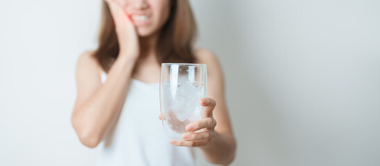 Teeth Sensitive to Cold concept. woman hold Ice Water glass and having toothache and pain after...