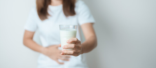 Lactose intolerance and Milk allergy concept. woman hold Milk glass and having abdominal cramps and pain when drink Cow Milk. Symptom stomach ache, Dairy intolerant, Nausea, Bloating, Gas and Diarrhea - obrazy, fototapety, plakaty