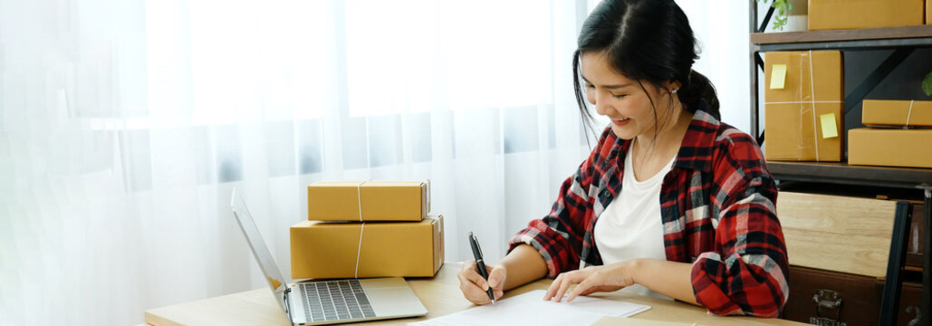 Banner Online seller Close up hands Young asian woman typing laptop keyboard checking online order on stock delivery package. Asian woman startup small business at home office with copy space