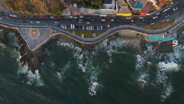 Aerial view of Mazatlan's winding Malecon, where cars drive in contrast to the beauty of the waves crashing against the city's distinctive rocky coastline.
