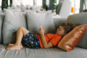 A boy with curly hair is deeply immersed in the game on the phone.