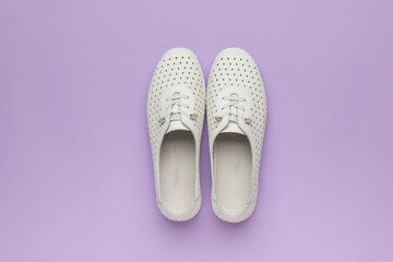 A pair of women's white athletic shoes on a purple background.