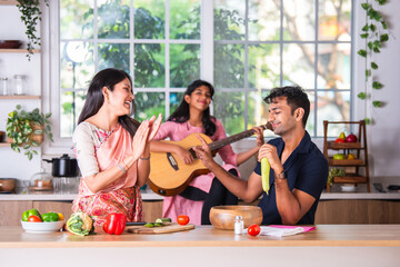 Indian family having fun while cooking playing and singing song on guitar