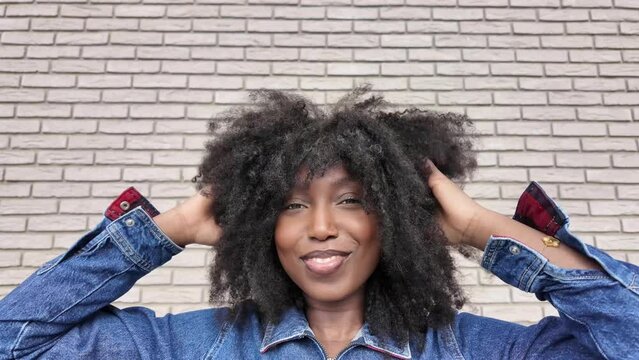 In this footage, a vibrant young black woman with afro-textured hair exudes confidence and joy in an urban setting. Her playful expressions and stylish denim attire reflect a carefree spirit and a