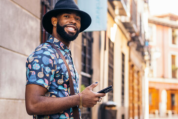 Stylish black man using smartphone outdoors in the city