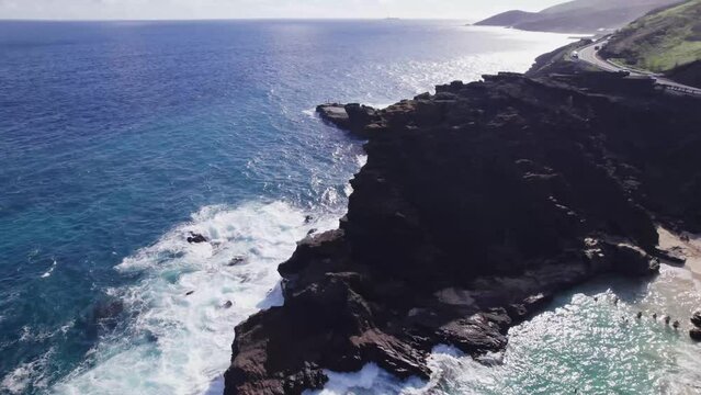 aerial footage circling around a rocky peninsula as white capped waves of the Pacific ocean crash along the rocky shore as the turquoise water sits peacefully in the secluded  Halona Beach cove