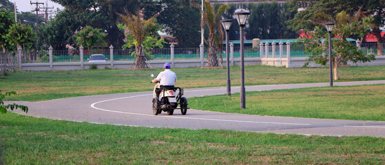An elderly person drives a three-wheeled scooter in the park.