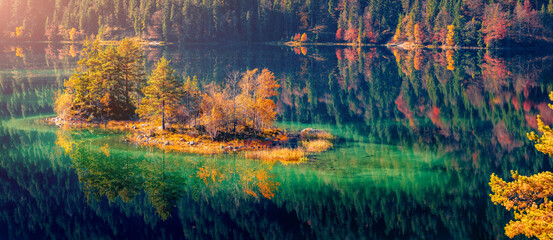 Calm autumn scene of Eibsee lake with small islet. Panoramic morning view of colorful foliage on...