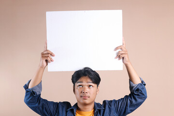 Young Man Looking Up to The Blank White Board Indicating Advertisement Mockup Isolated on Beige...