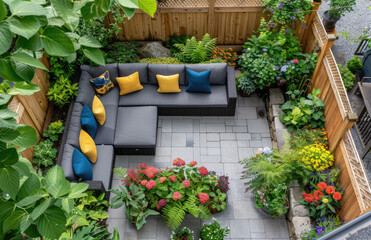 A photo of an urban backyard garden with colorful outdoor furniture, lush green plants and flowers, grey pavers in the yard, a wooden fence
