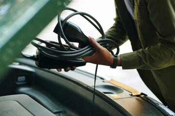 Closeup image of electric car driver putting charging cable in trunk