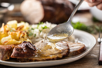 A close-up view of a spoon with sauce that pours over the meat, roasted neck. As a side dish to the meat are baked potatoes and jasmine rice.
