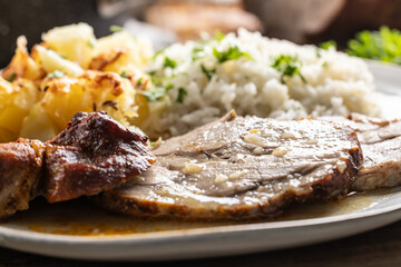 A portion of baked juicy neck on a plate with a side dish of potatoes and rice and a sauce with baked goods - 791296769
