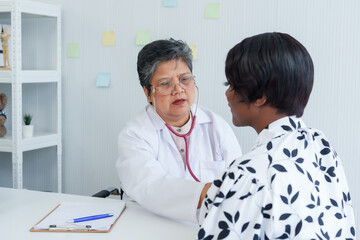 Obstetrician in white coat discusses health with attentive patient, both seated at clinic desk,...