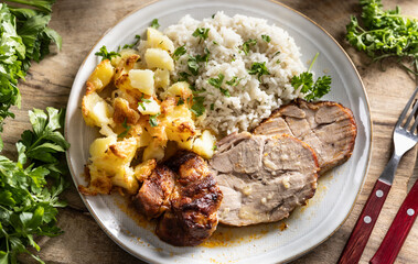 A portion of baked juicy neck on a plate with a side dish of potatoes and rice and a sauce with...