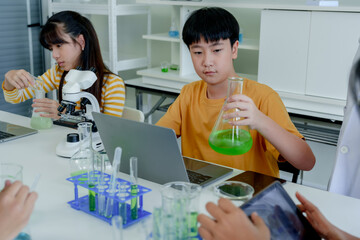 Students' learning in science classroom. Girl in striped yellow top performs science experiment,...