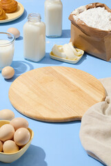 Empty wooden chopping board arranged with lots of eggs, fresh milk, baked bread and a dish of butter. A paper bag of flour decorated. Product can be displayed on the cutting board for promotion