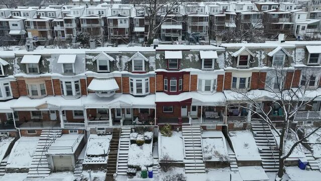 Colorful row homes in urban American city at snowy winter day. Rundown low income housing in USA. Rising drone wide shot.