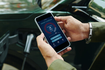 Electric car driver checking smart charger application on smartphone