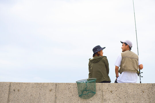 釣りをしながら堤防に座って話す男女
