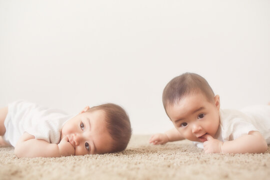 ベージュのラグに寝転んで指吸いをする双子の赤ちゃん