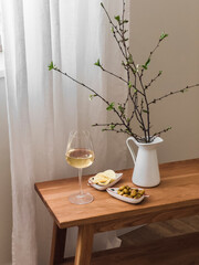 Delicious homemade aperitif - a glass of white wine, potato chips, grilled olives on a wooden bench by the window in the living room - 791308565