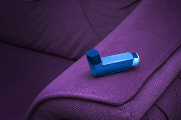 The asthma inhaler on the purple sofa. Medicine for people with shortness of breath. Healthcare and medical concept. - obrazy, fototapety, plakaty