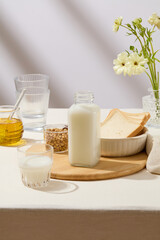 Unlabeled bottle of milk, a cup of soybeans and a bowl containing sandwiches placed on a cutting board. A jar filled with honey and a flower pot decorated. Branding mockup