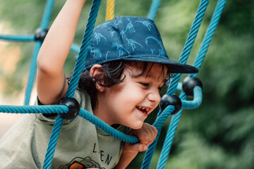 A joyful child climbs a rope ladder, his smile bright and carefree during a vibrant playtime