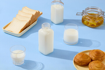 On the blue surface, some bottles and cups of milk are displayed with a jar containing ginger jam. A dish of sandwiches and a dish of bread are featured. Breakfast content