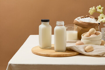Fototapeta na wymiar A table with tablecloth features some ingredients for baking such as eggs, flour and milk. A wooden chopping board with two blank label milk bottles displayed on for product promotion