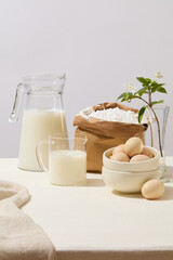 Front view of baking ingredients such as milk, a lot of eggs and a paper bag containing flour. A beautiful pot of flowers decorated. Empty space in the middle for product presentation