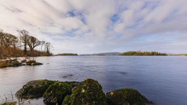 Time lapse of a rocky shore foreground with forest in distance on a cloudy sunny day at Lough Key in county Roscommon in Ireland.